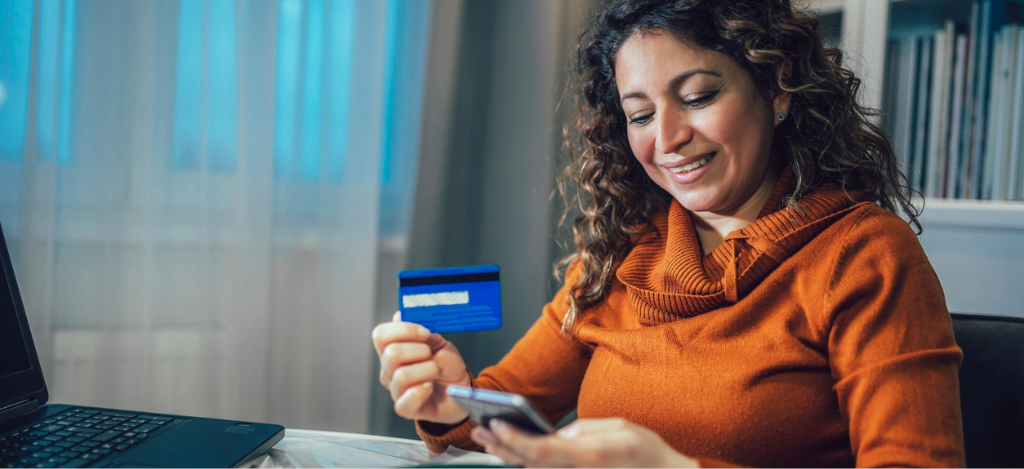 A woman at home holding her credit card and smartphone while paying for her medical bill online.