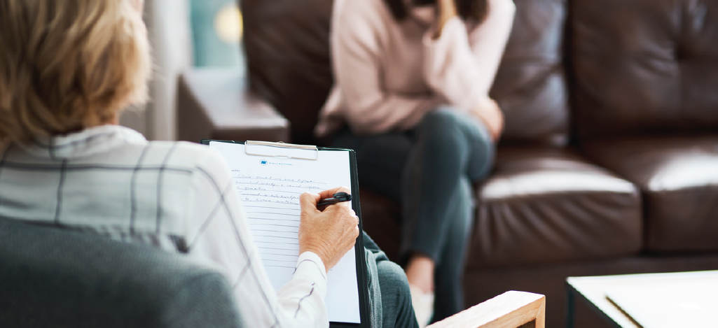 Mental health billing compliance - A female psychologist taking notes during a counseling session with her female client.