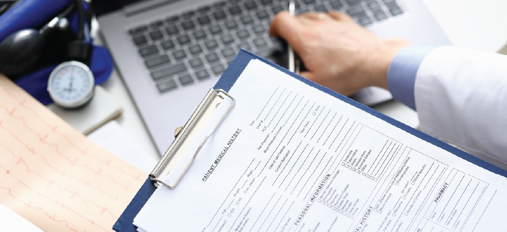 Avoiding common medical billing errors - A male doctor holding a patient information form while checking his laptop.